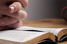 hands folded over a Bible